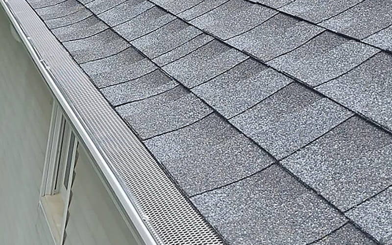 Closeup photo of a newly replaced gutter on a light green New Jersey house with gray shingle roof.