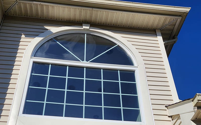 Photo looking up at a large, grand arch-shaped window recently installed on a cream-colored New Jersey home by Everest Construction Group.